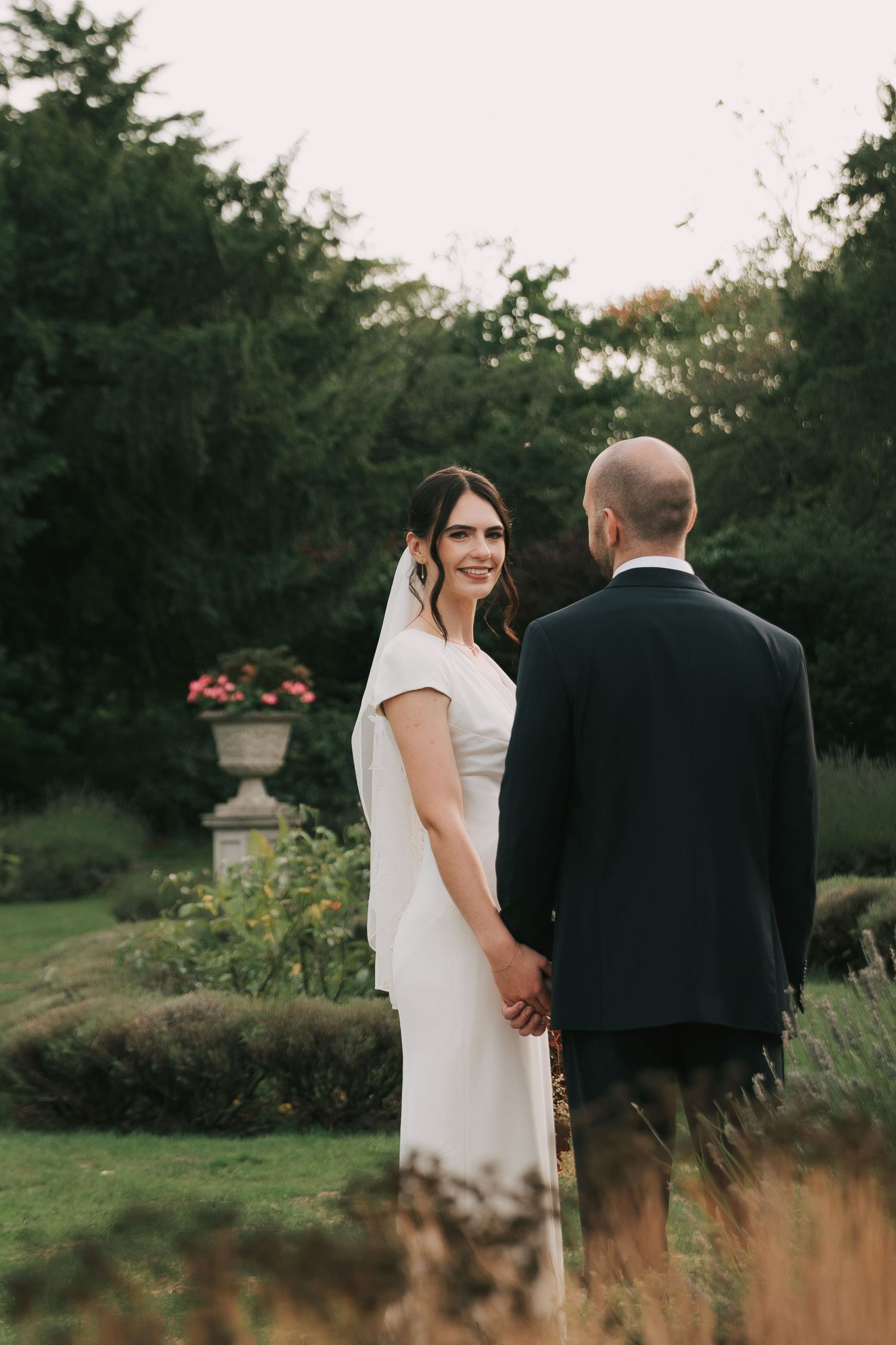 Newlywed couple strolling through a garden at sunset with rustic landscaping.