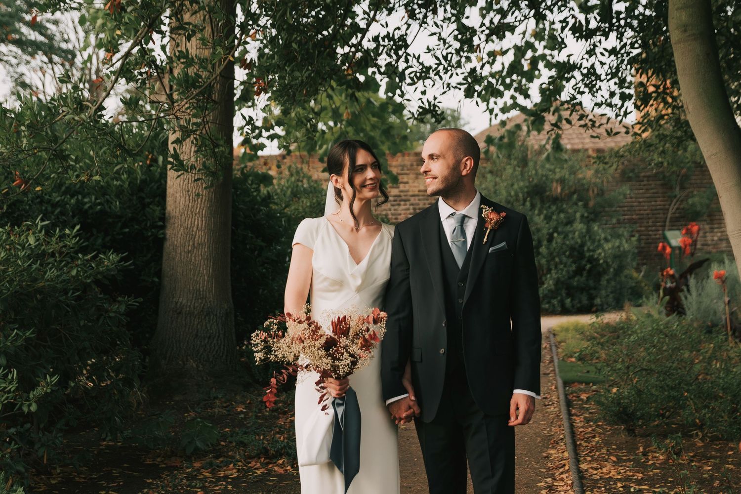 Couple walking together through autumn foliage in an outdoor garden setting.