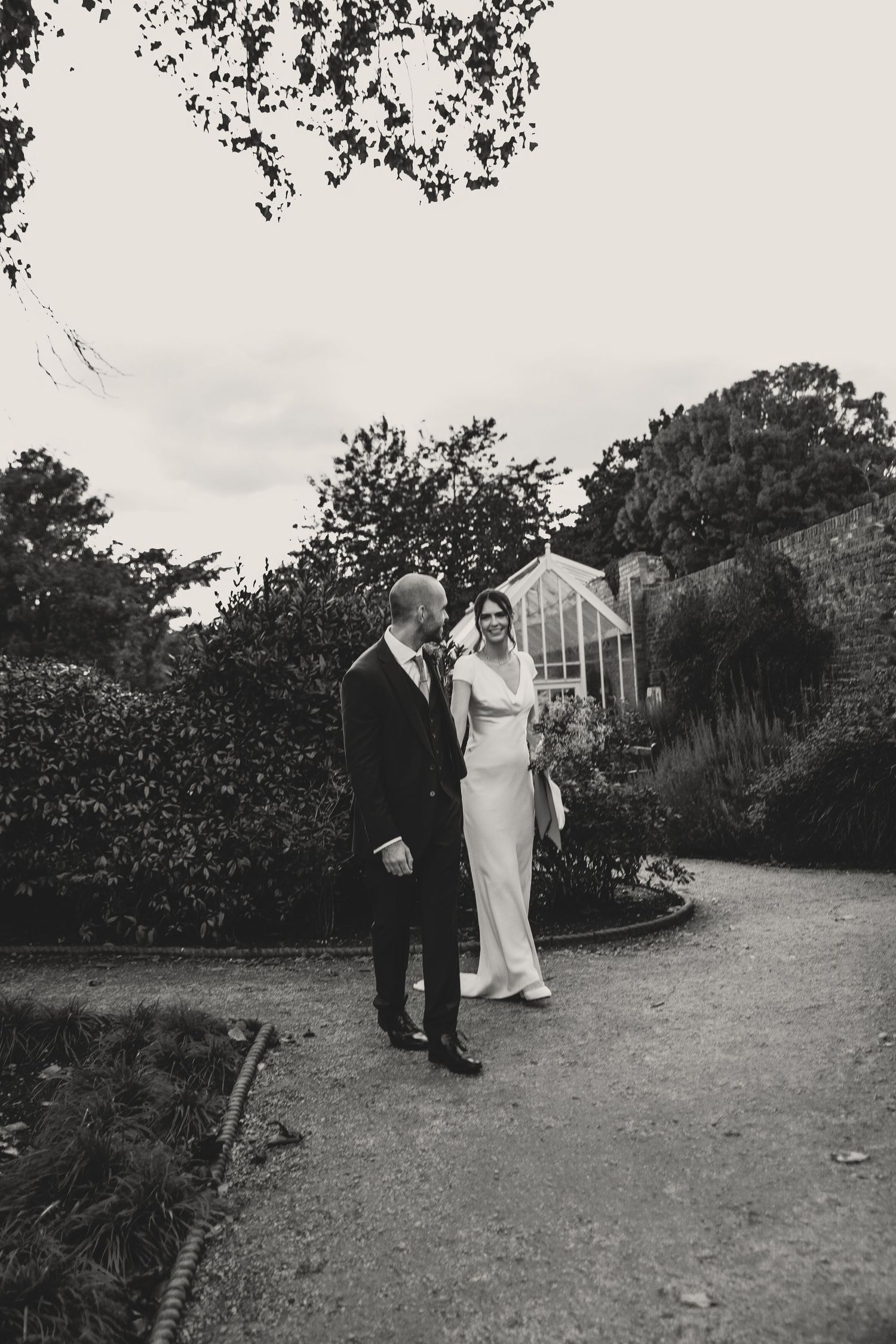 Black and white photo of a couple strolling through a garden landscape during their wedding day.