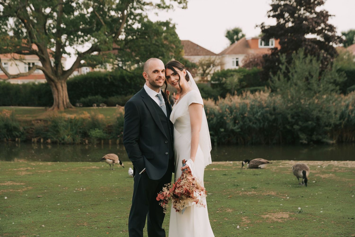 Newlyweds share an intimate moment on a grassy lawn during their outdoor wedding photoshoot.