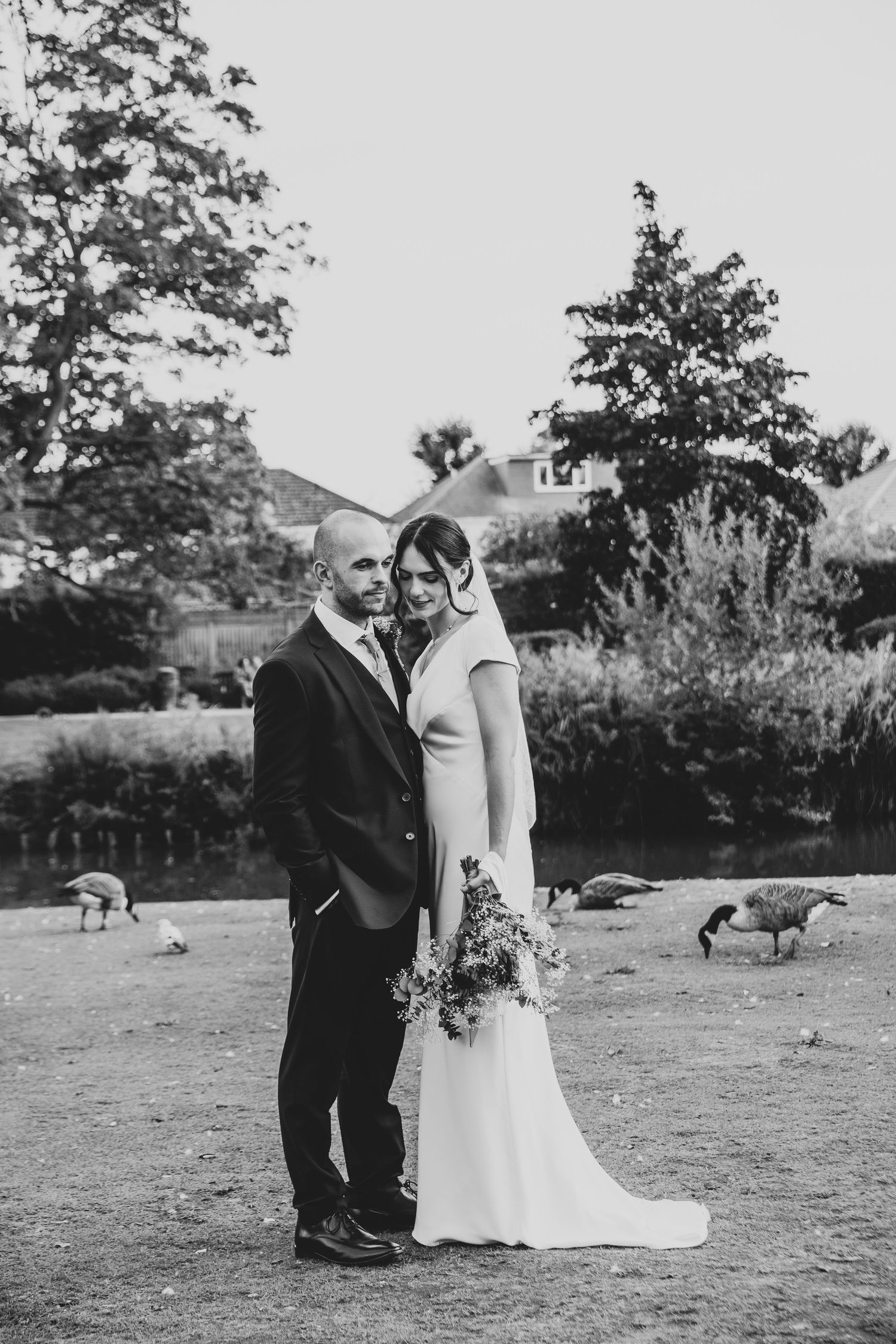 A black and white wedding portrait in a garden setting with geese wandering in the background.