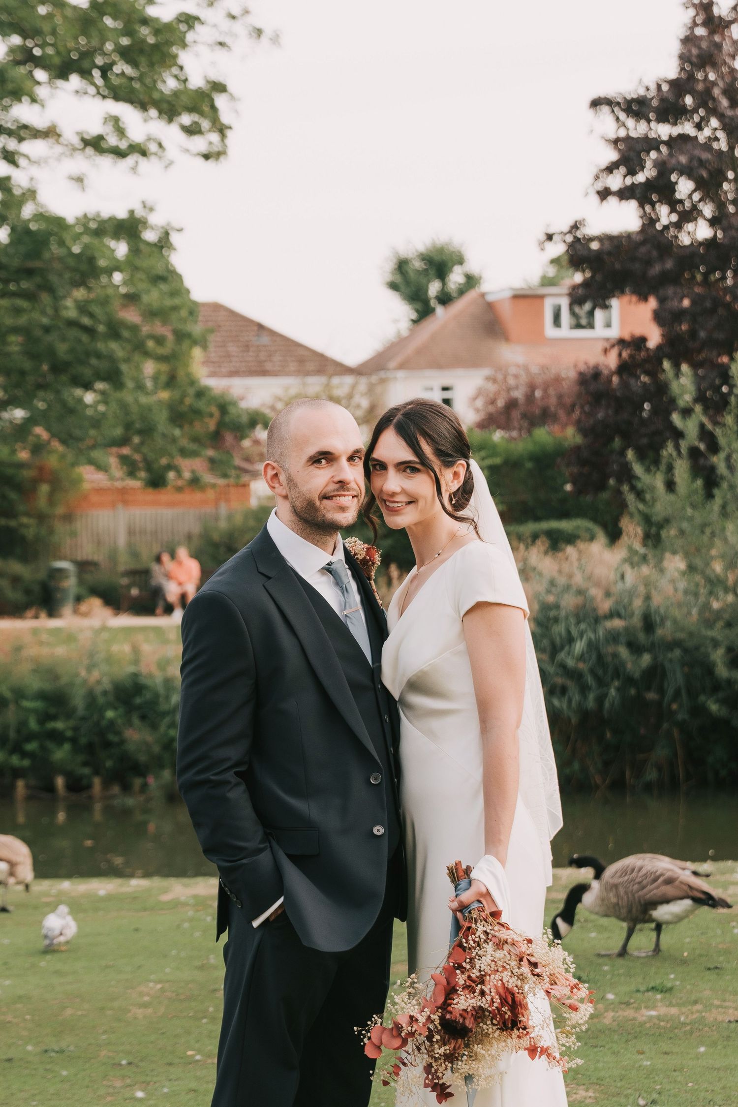 Elegant wedding portrait in garden setting with pond and geese in background.