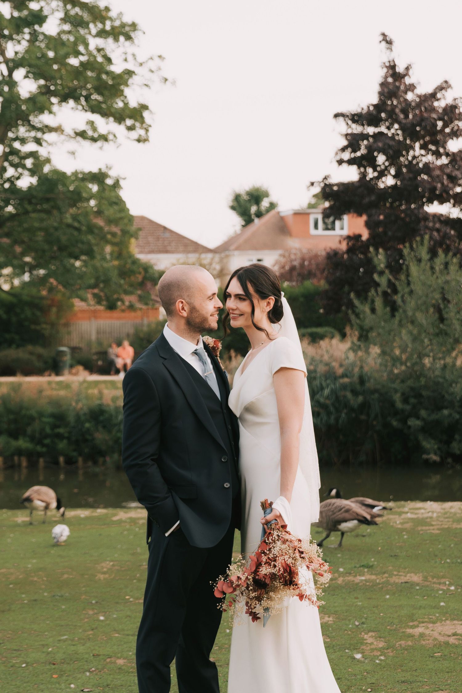 A romantic wedding couple shares tender moments in a garden setting with autumn trees in the background.