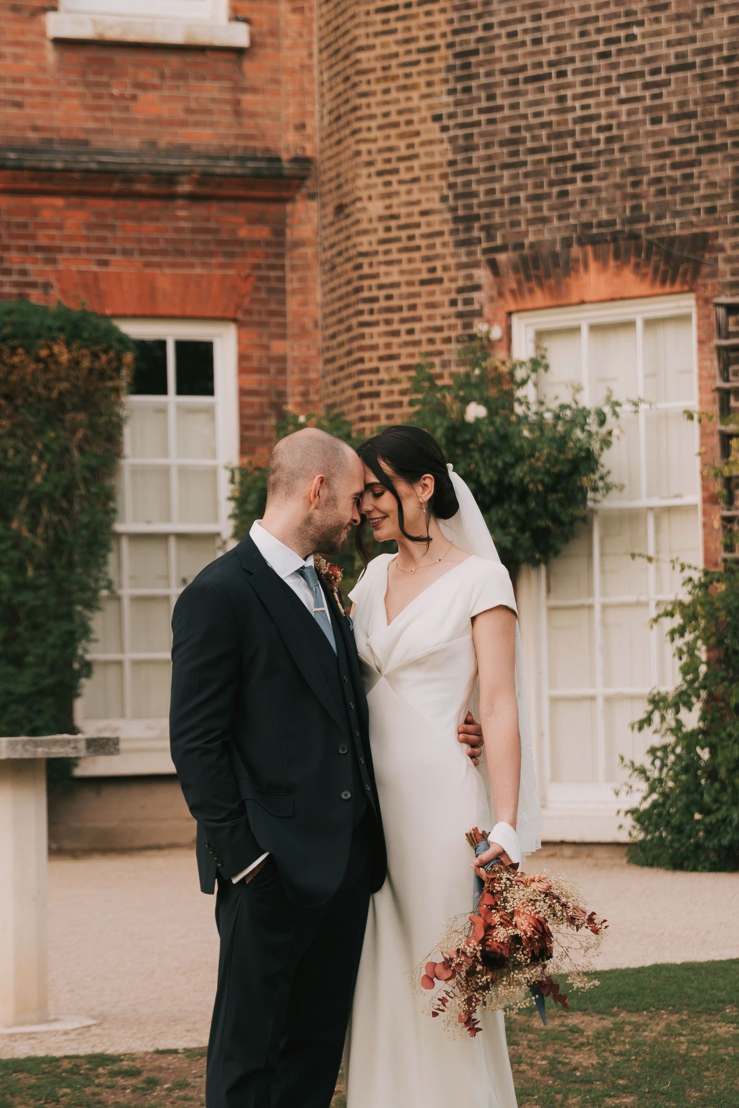 An intimate wedding moment captured against a historic brick building with white window frames.