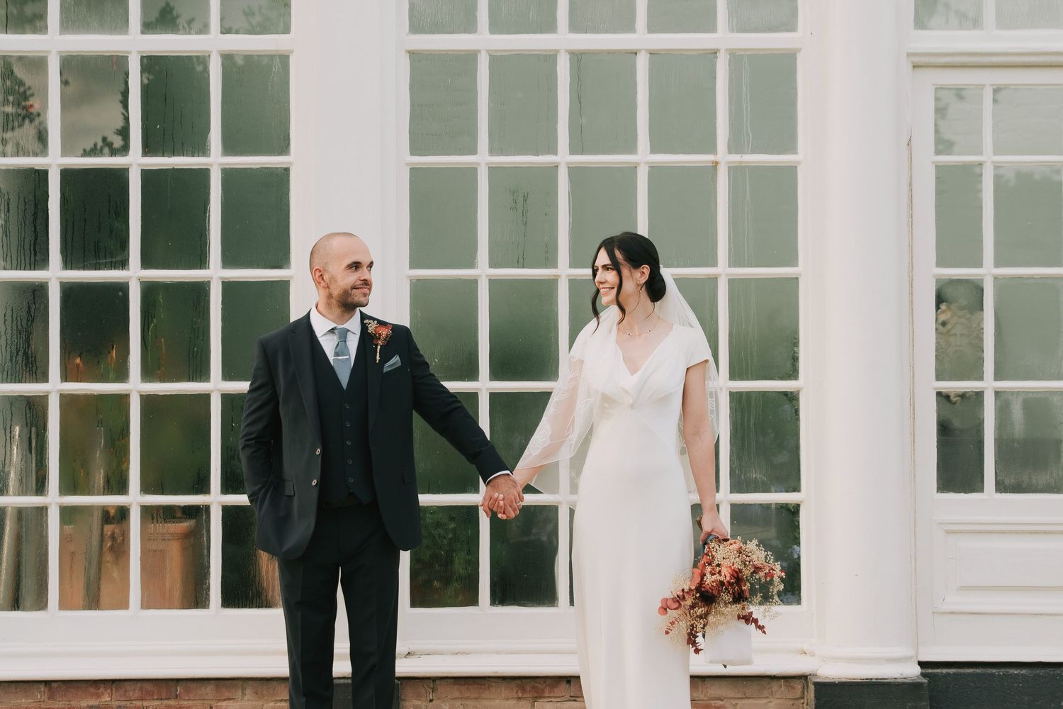 A wedding couple and their bridal party pose in front of white windows in an elegant indoor setting.