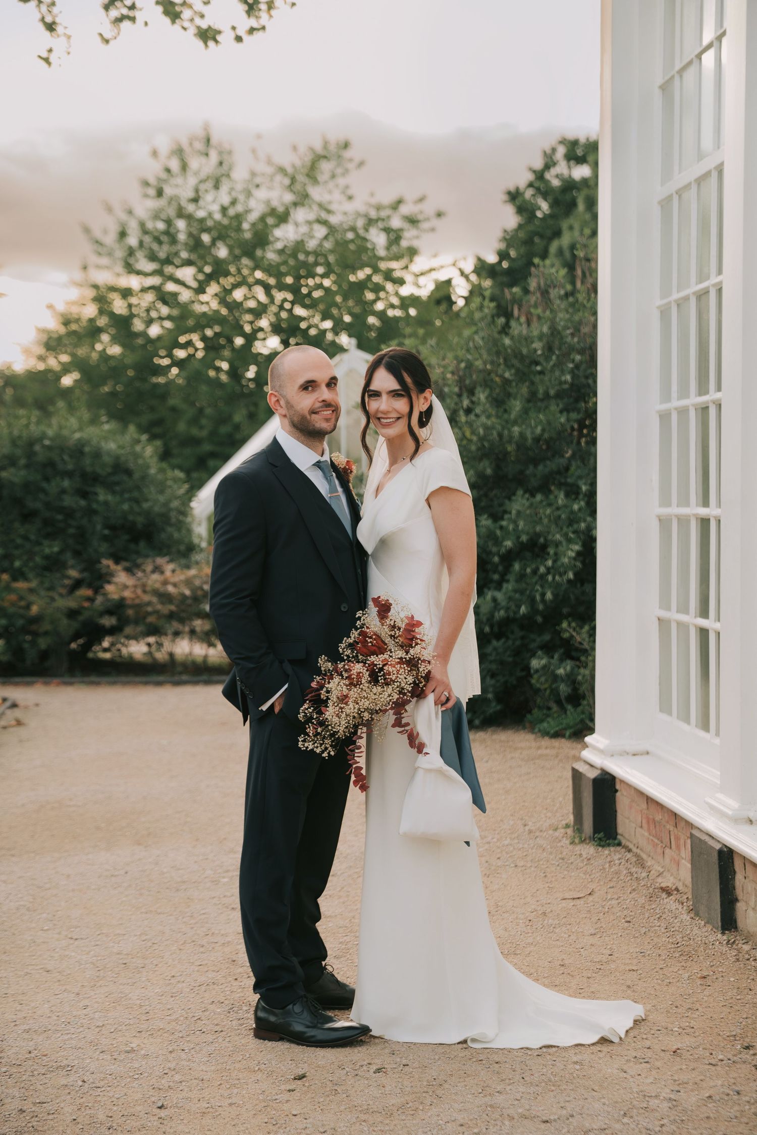 A romantic wedding portrait captured at sunset against white colonial architecture and lush gardens.