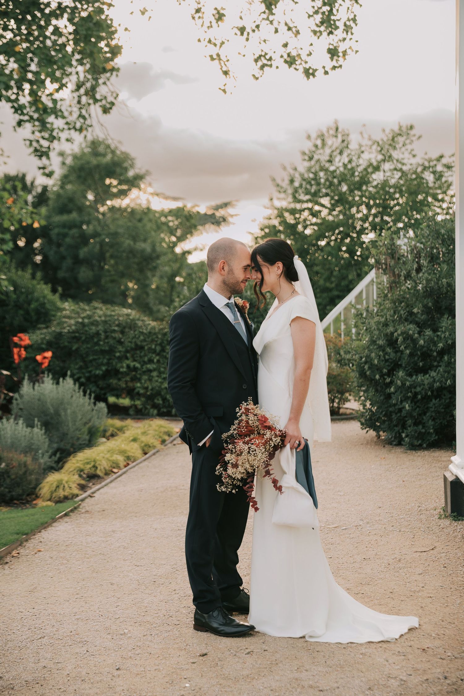 A romantic sunset garden wedding portrait with dried flower bouquet and elegant attire.