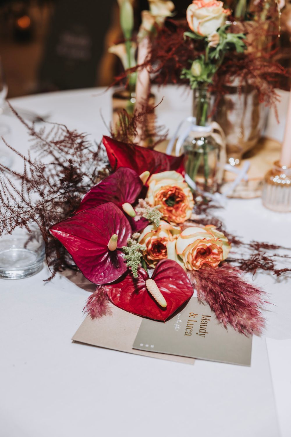 Bridal bouquet  of deep burgundy anthurium flowers with dried pampas grass and coral roses laid casually on a table