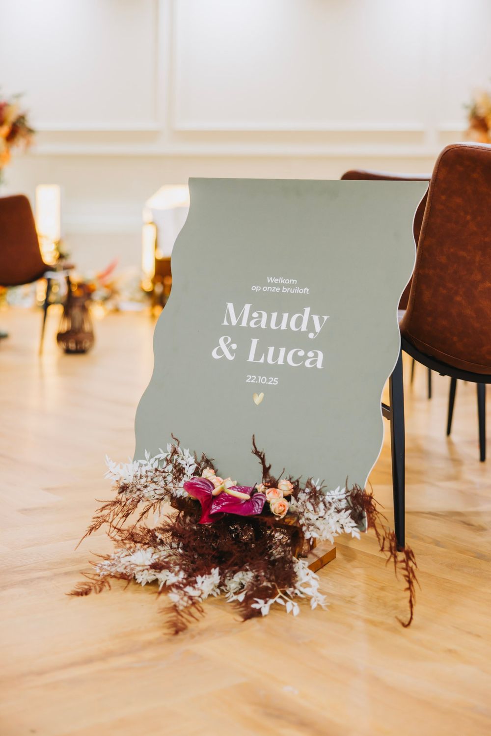 Wedding signage for displayed with dried flowers and pink accents on a wooden floor.