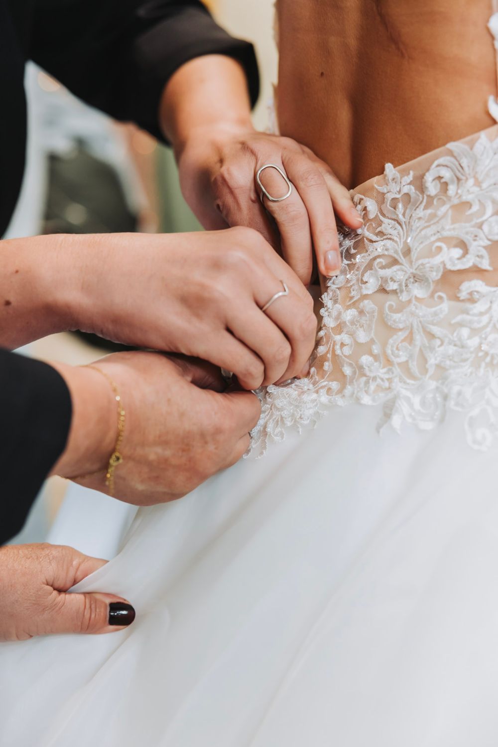 Hands fastening delicate white lace buttons on a wedding dress in a closeup detail shots.