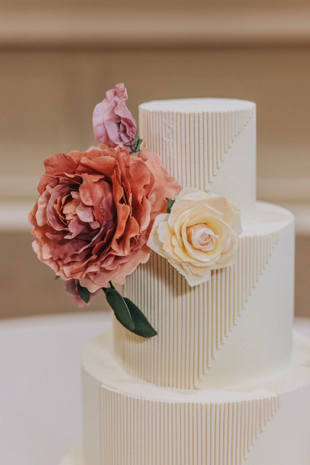 Elegant white wedding cake decorated with textured stripes and dusty rose and cream colored flowers.