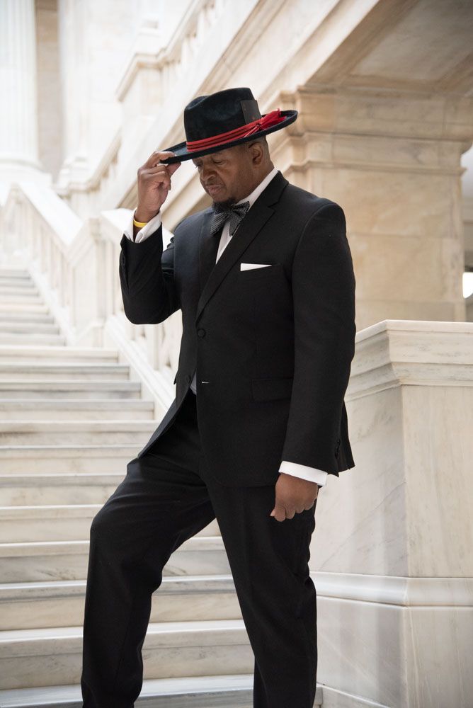 Two people in formal black attire pose on grand marble staircase.