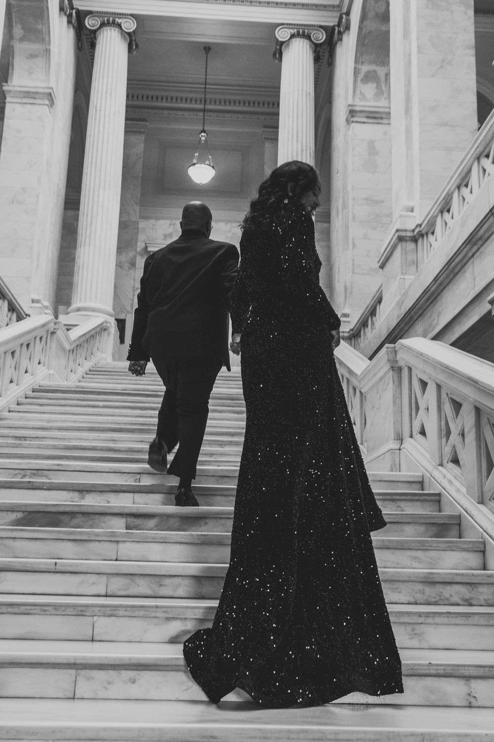 Silhouettes of people ascending elegant marble staircase in formal wear.