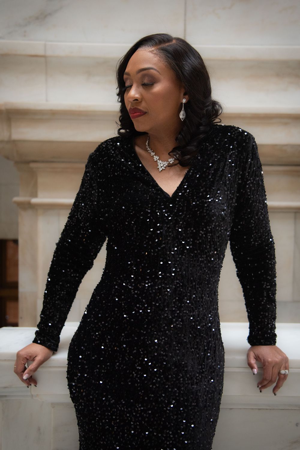 A figure in a sparkling black evening gown poses against a light-colored wall in a series of glamorous shots.