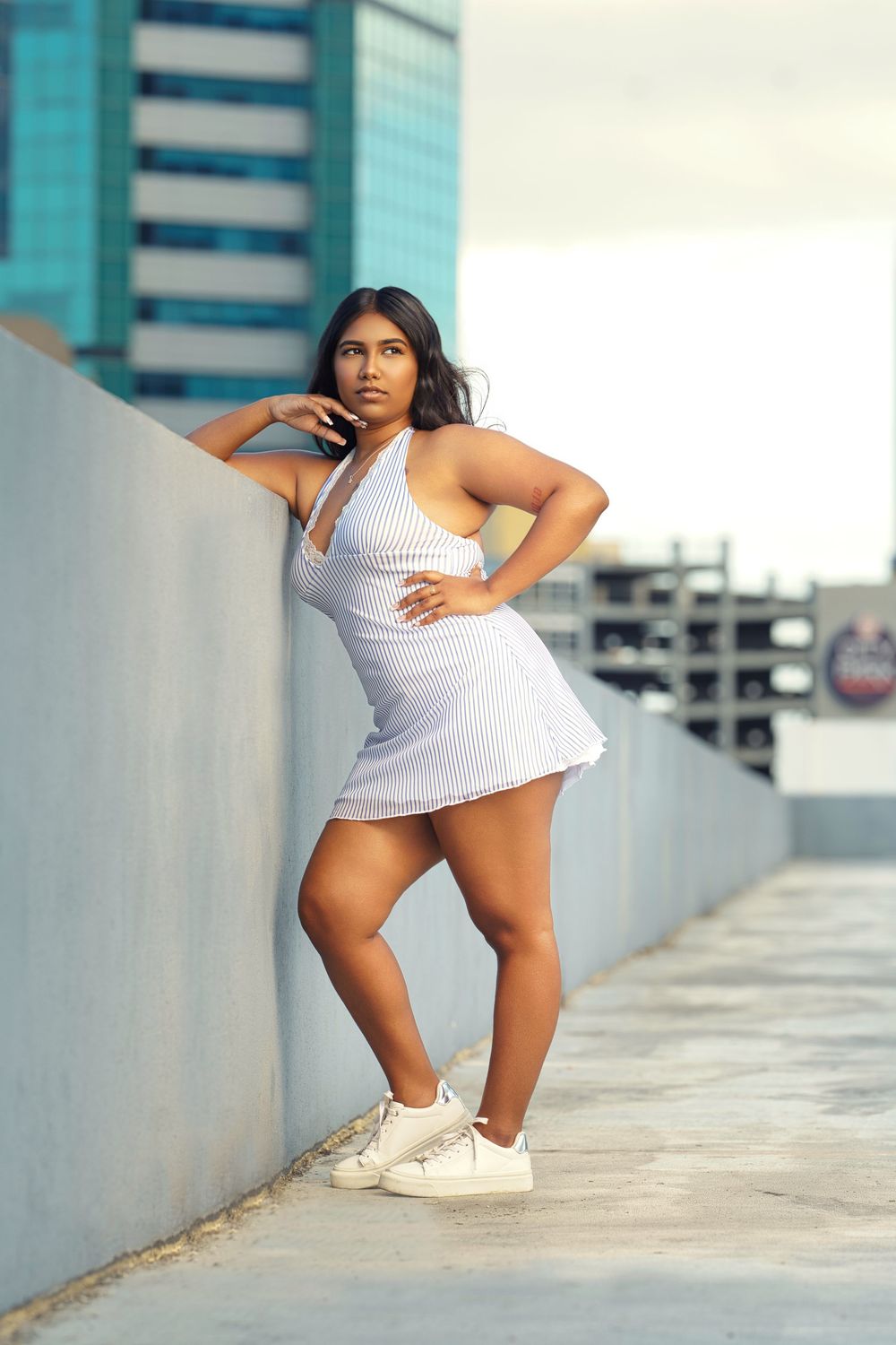 Athletic figure in white tennis dress and sneakers poses dynamically in an urban parking structure.