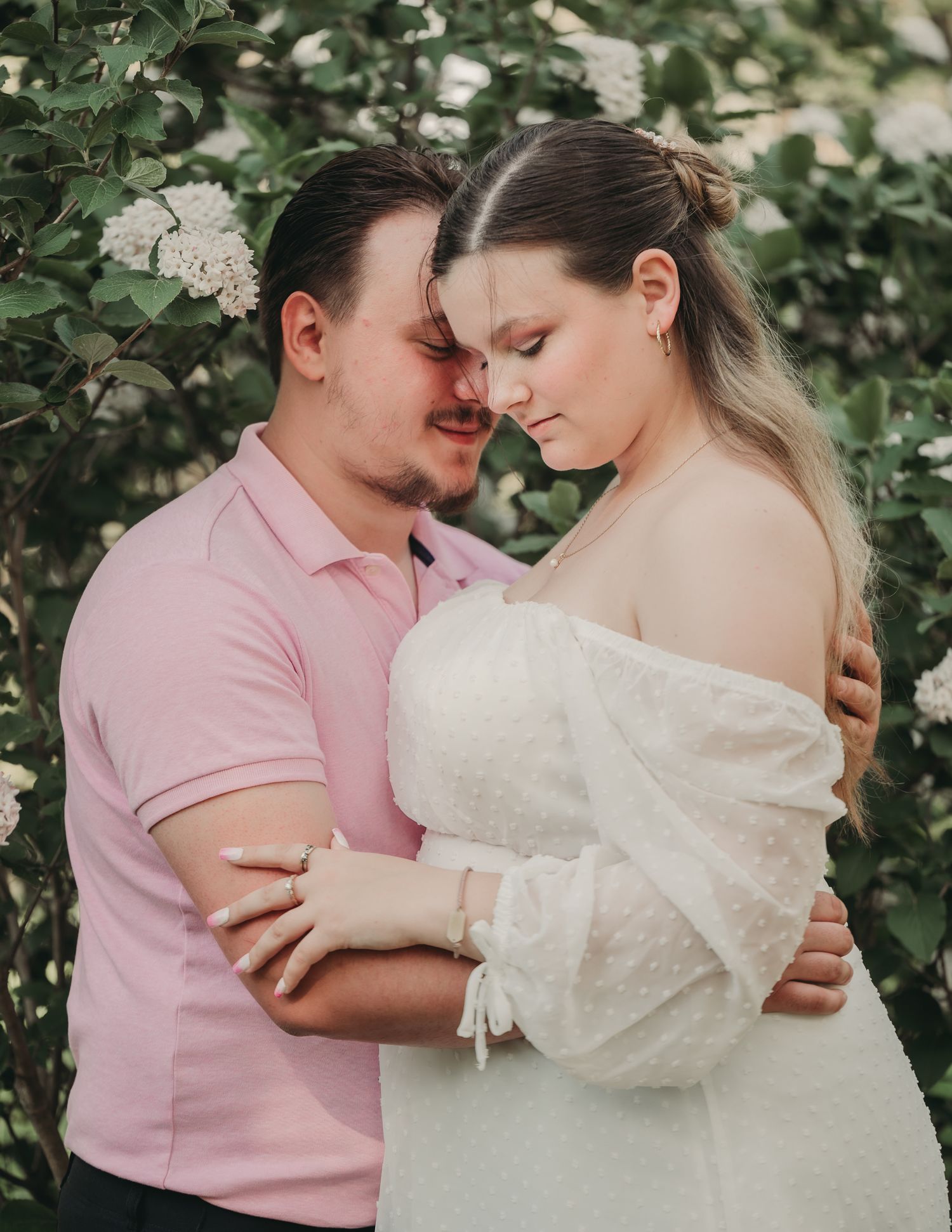 An intimate engagement photo of a couple in soft lighting among white flowering bushes.