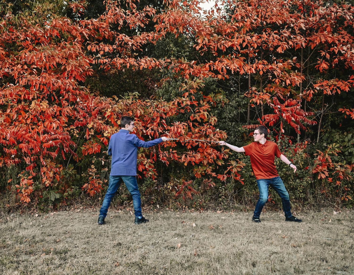 Two children playing and reaching out against vibrant red fall foliage.