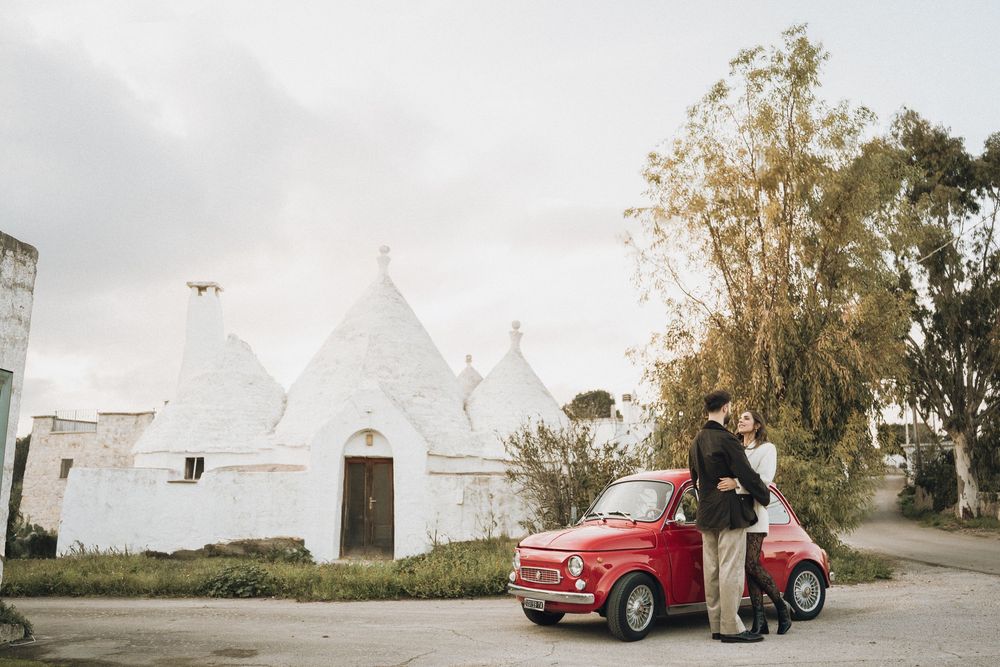 A series of vintage cars parked in front of white buildings against a cloudy sky during a wedding photo session.