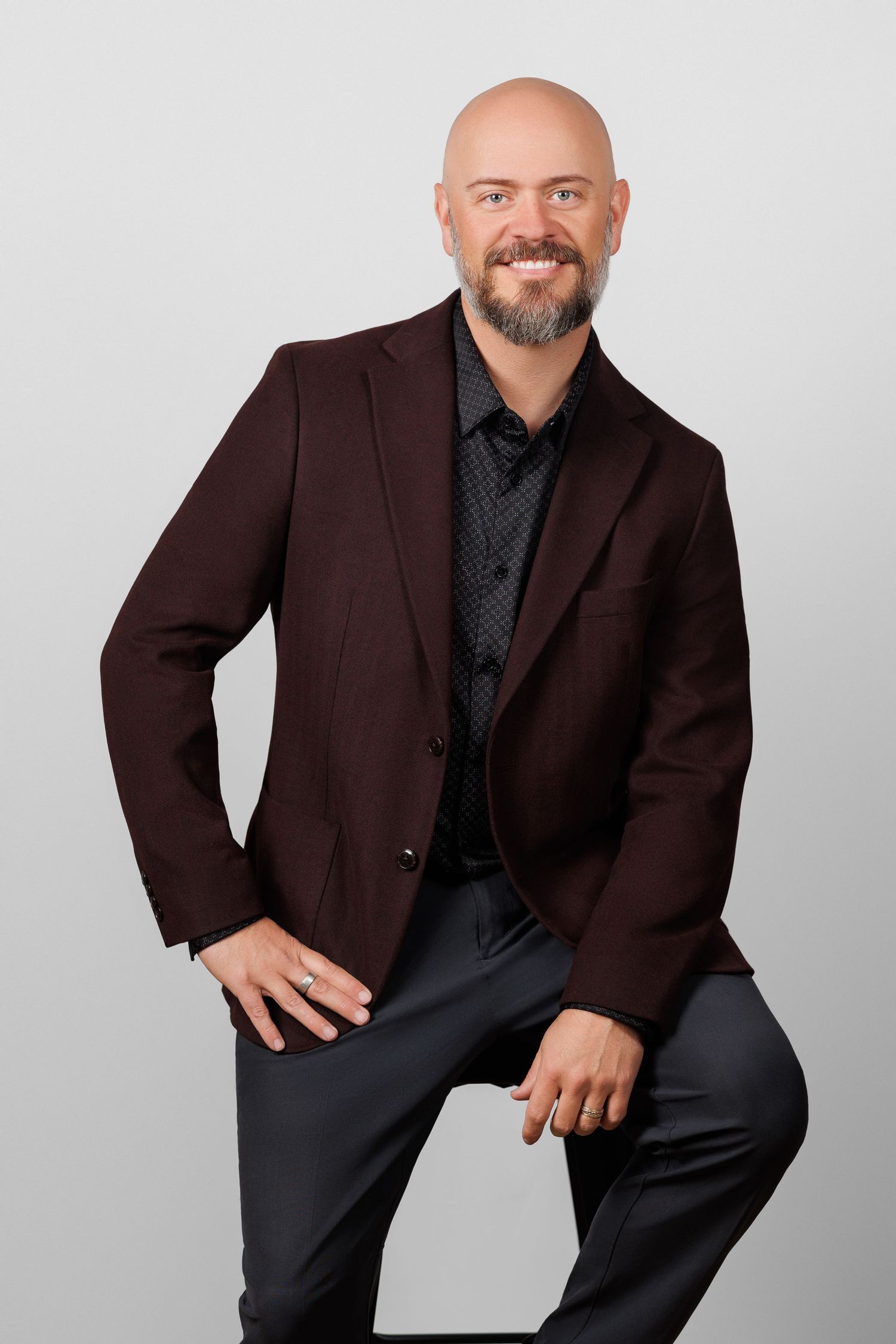 Professional headshot portrait of someone in glasses and black blazer with warm smile against grey backdrop.