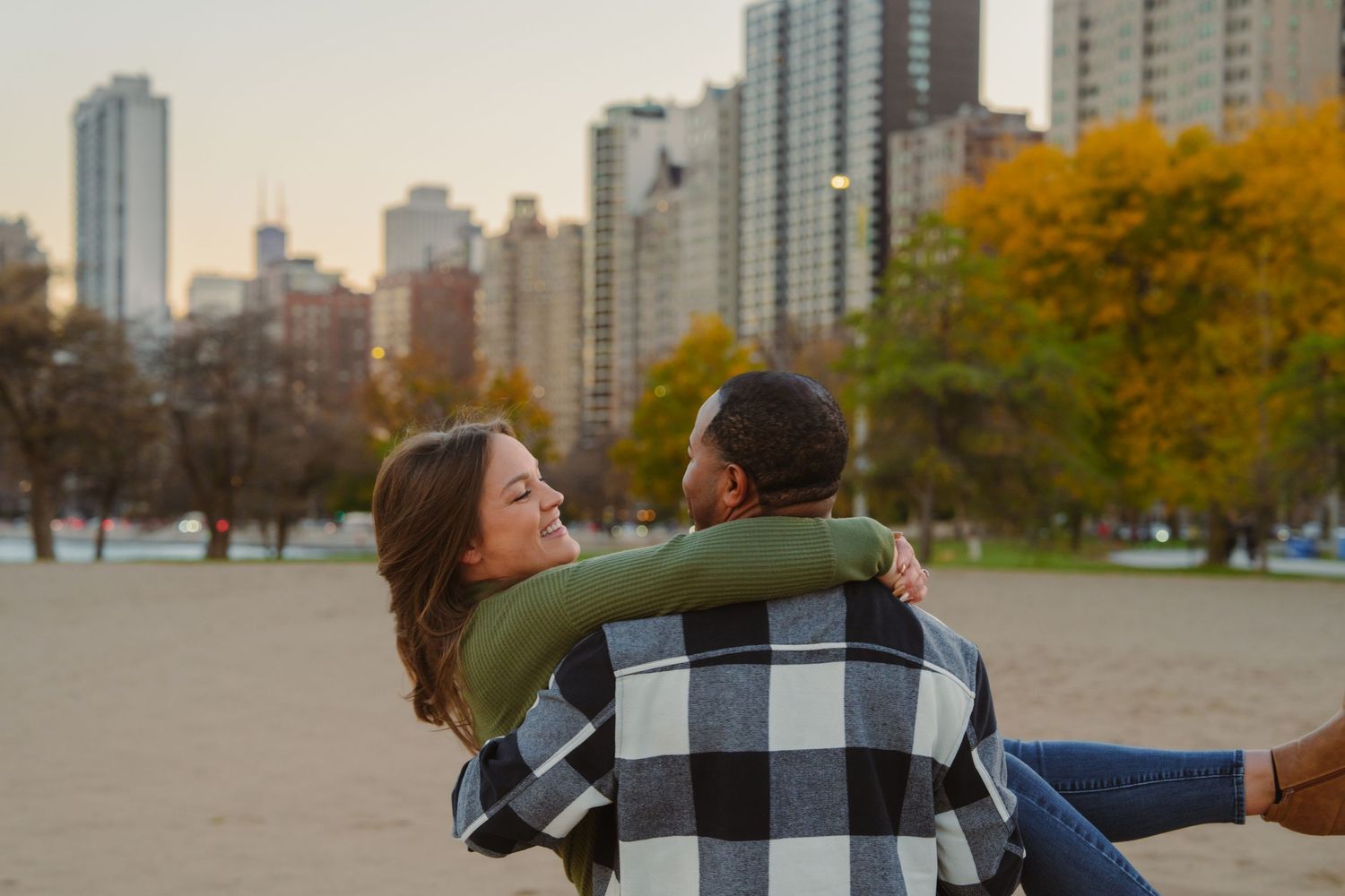 Couple enjoying autumn day in park with city skyline in background.