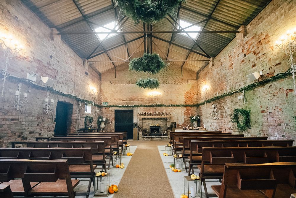 The Oakley Barn - Rustic brick wedding venue interior with wooden chairs, aisle runner and hanging greenery in an industrial-style space.
