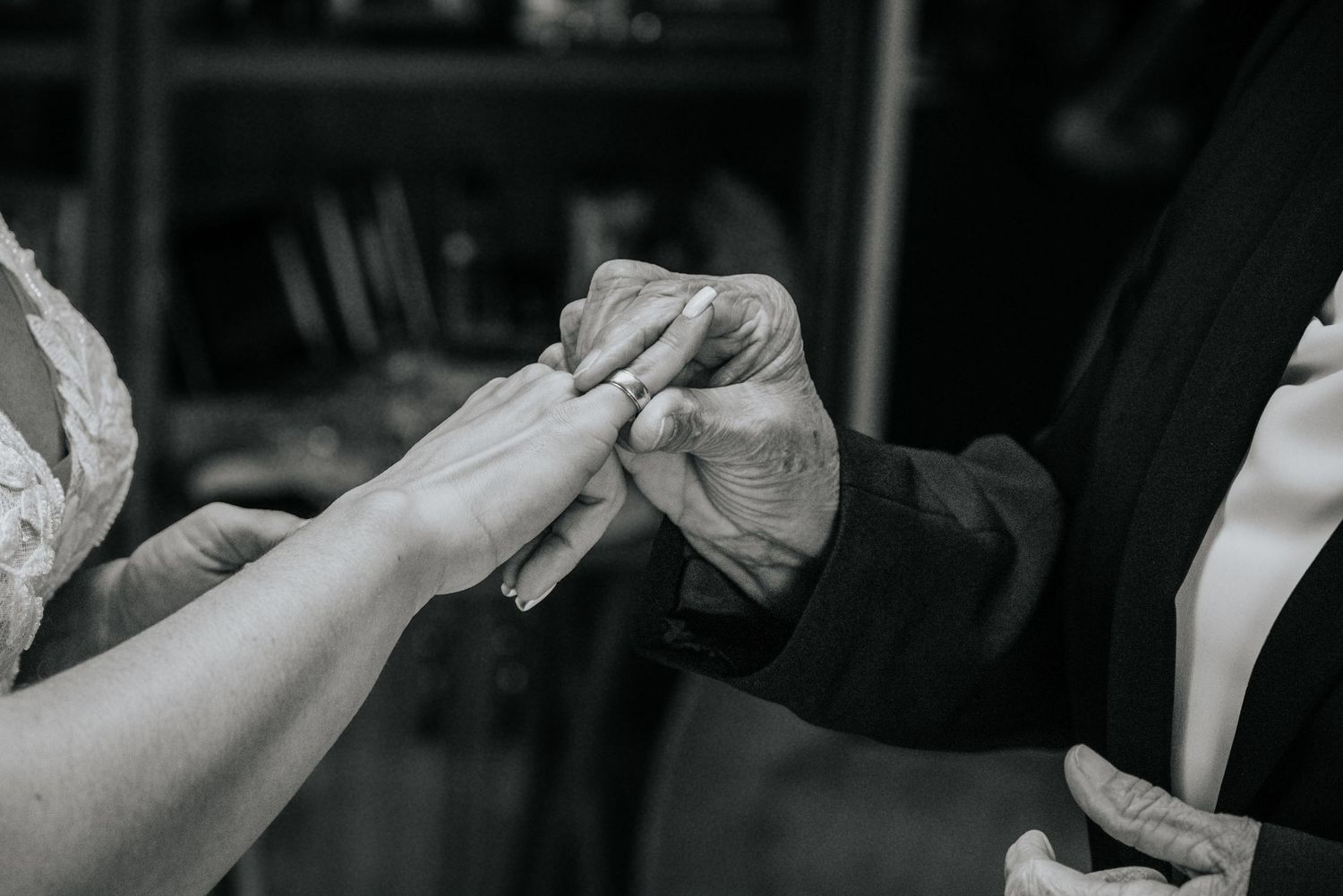 Black and white close-up of couple exchanging wedding rings during intimate ceremony.