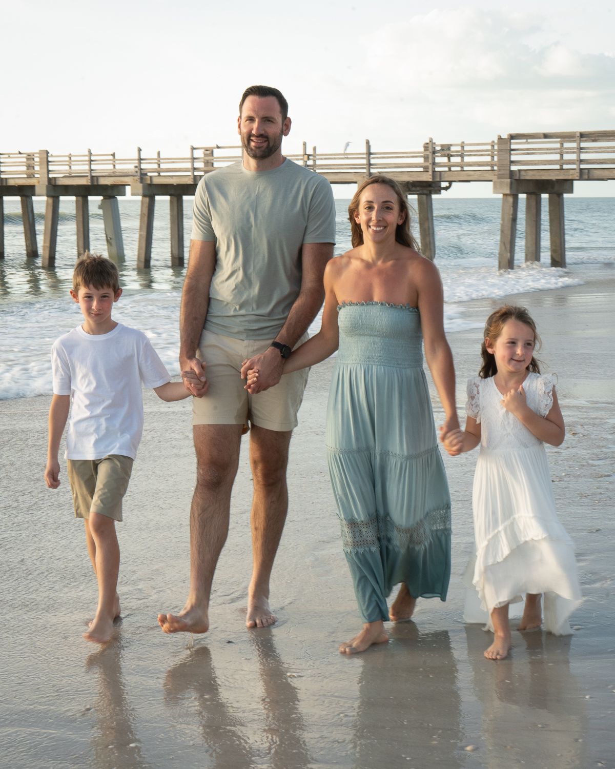 Family walking together along the beach shoreline at sunset wearing coordinating blue and white outfits.