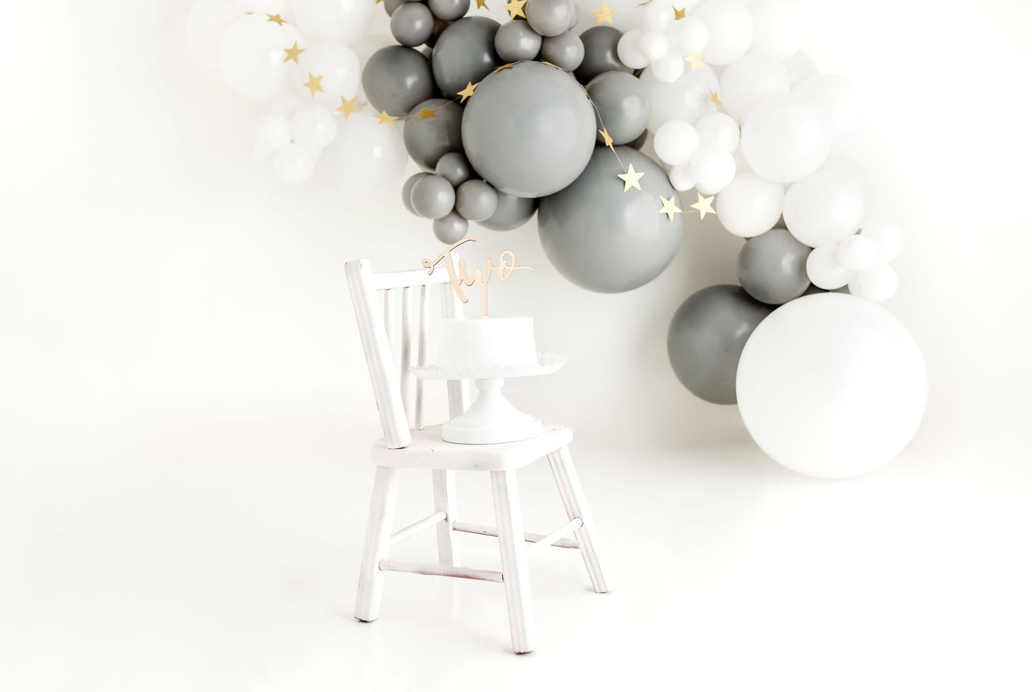 White chair with gray and white balloon arch and floral decorations.