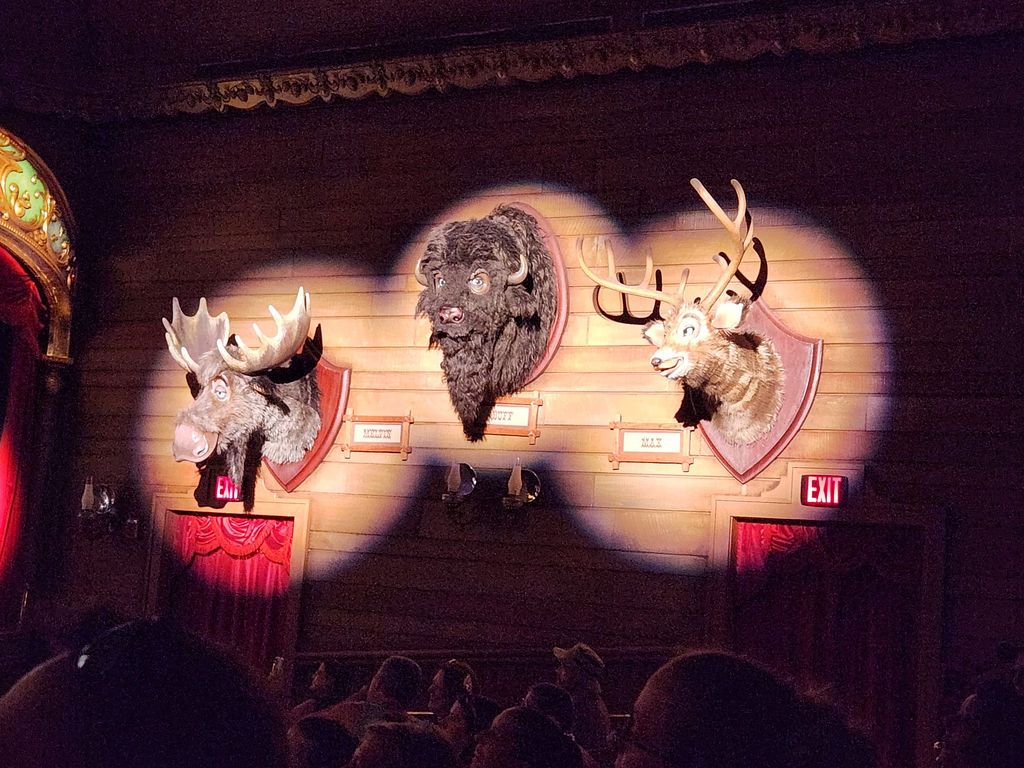 Three mounted deer head trophies illuminated by spotlights on a rustic wooden wall in a dimly lit interior space.