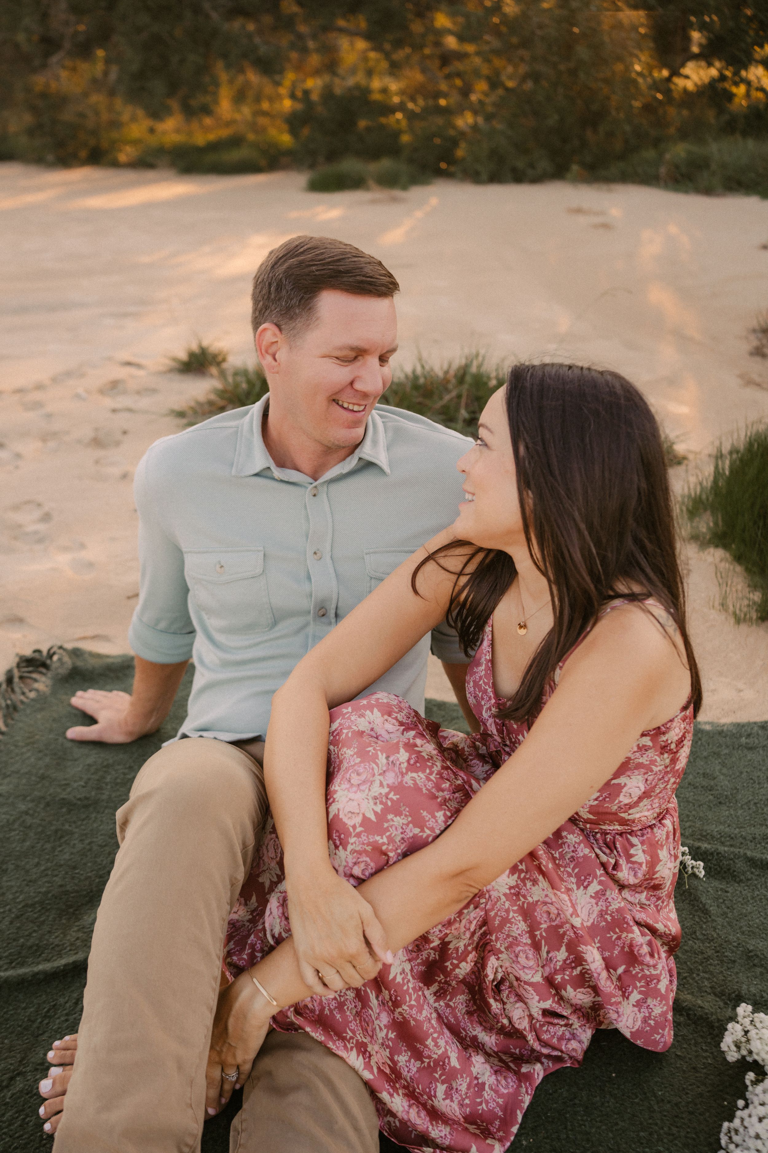 A couple shares a tender moment sitting together outdoors during golden hour sunset on a dirt path.