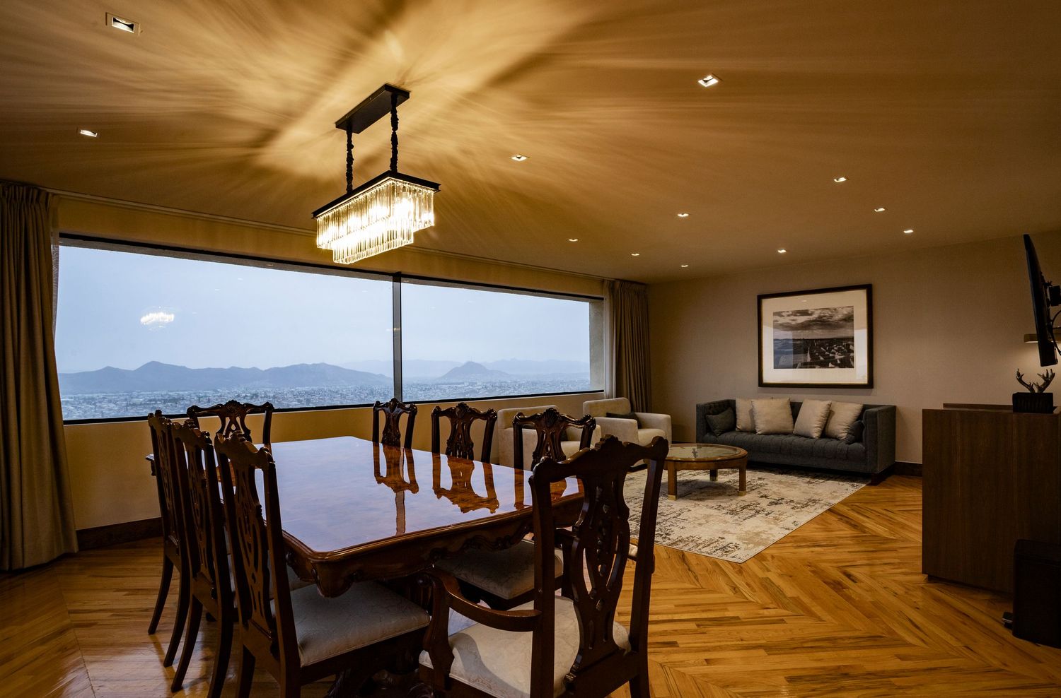 Elegant dining room with wooden table, mountain views through large windows, herringbone parquet floors, and modern chandelier.