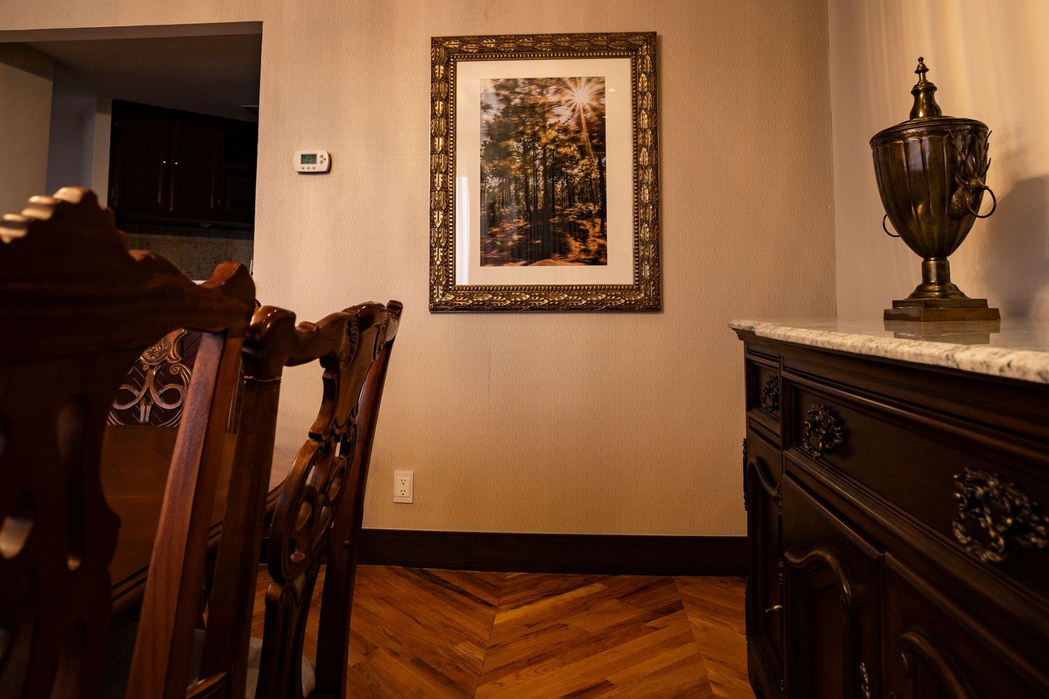 Elegant dining room with dark wood furniture, herringbone parquet floors, framed autumn artwork, and ornate decorative urn on sideboard.