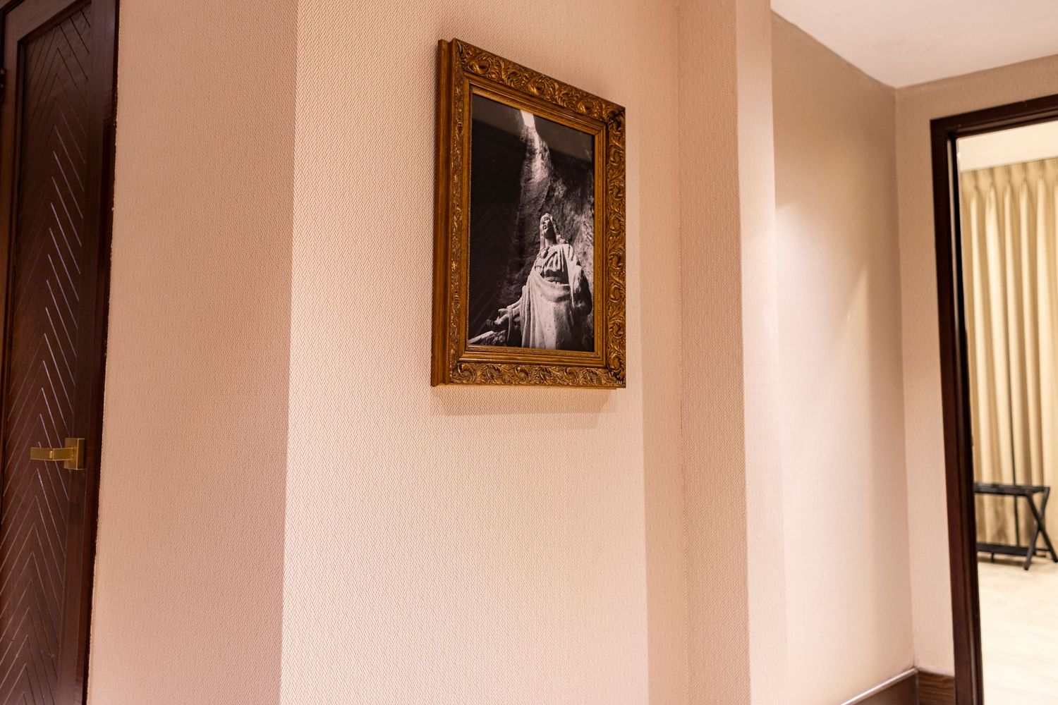 A hallway with beige walls featuring a gold-framed black and white wedding photo, with a wooden door on the left.