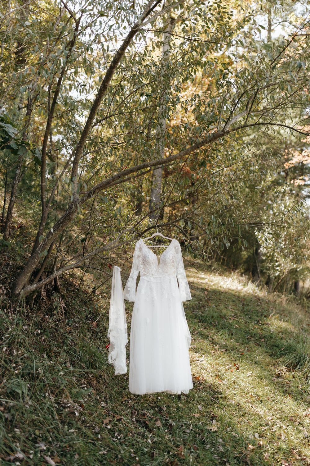 White wedding gown with long sleeves displayed outdoors among autumn trees and golden sunlight.