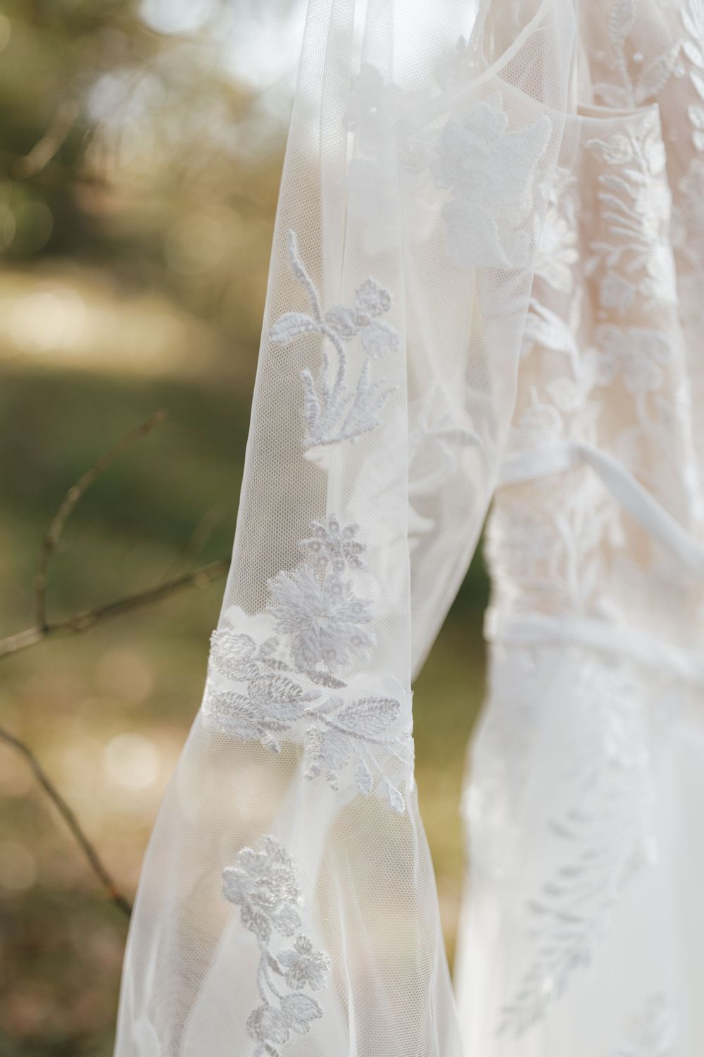 Delicate lace floral details on white wedding dress sleeve captured in soft natural light.