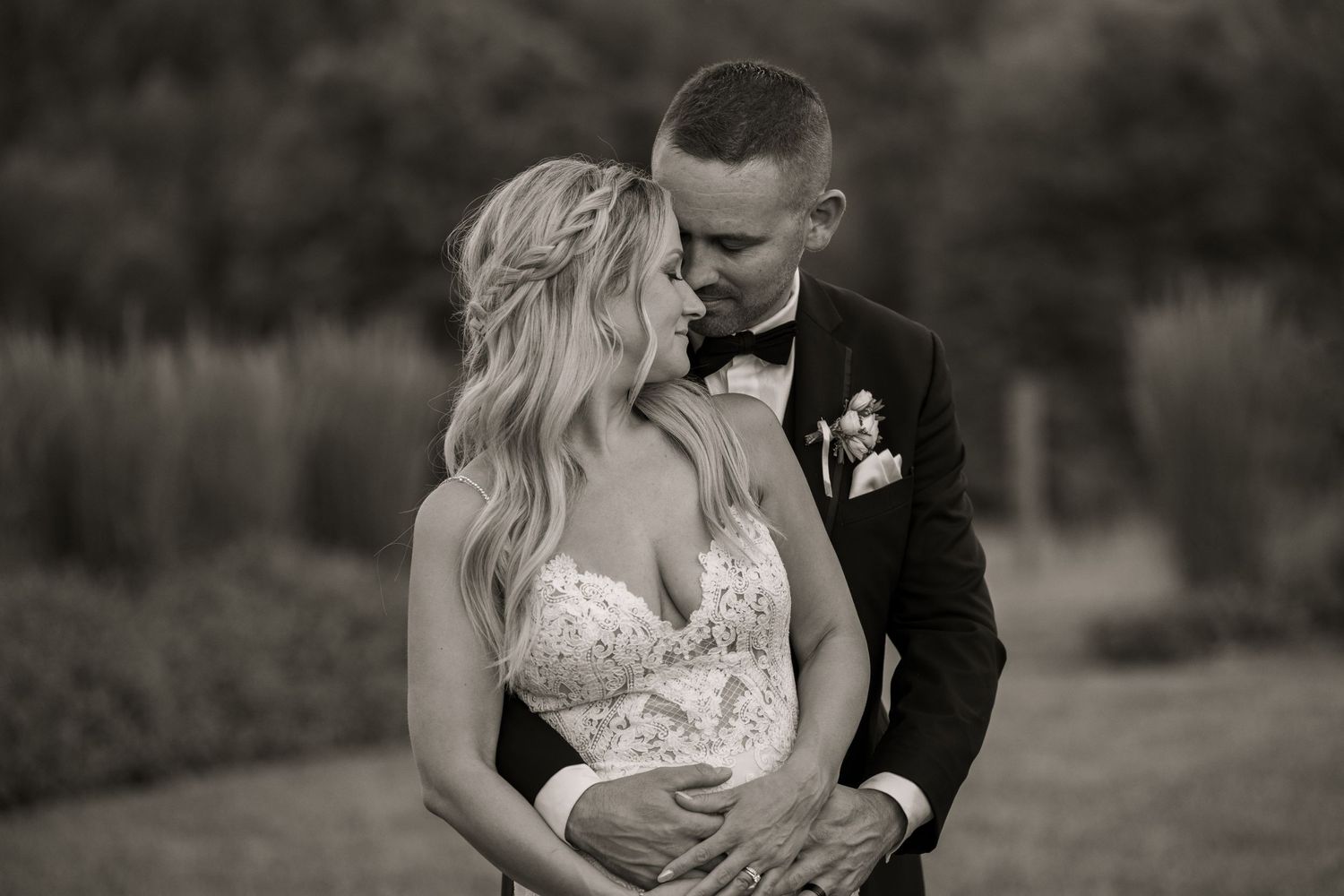 A romantic black and white wedding portrait shows a couple embracing on a garden path.