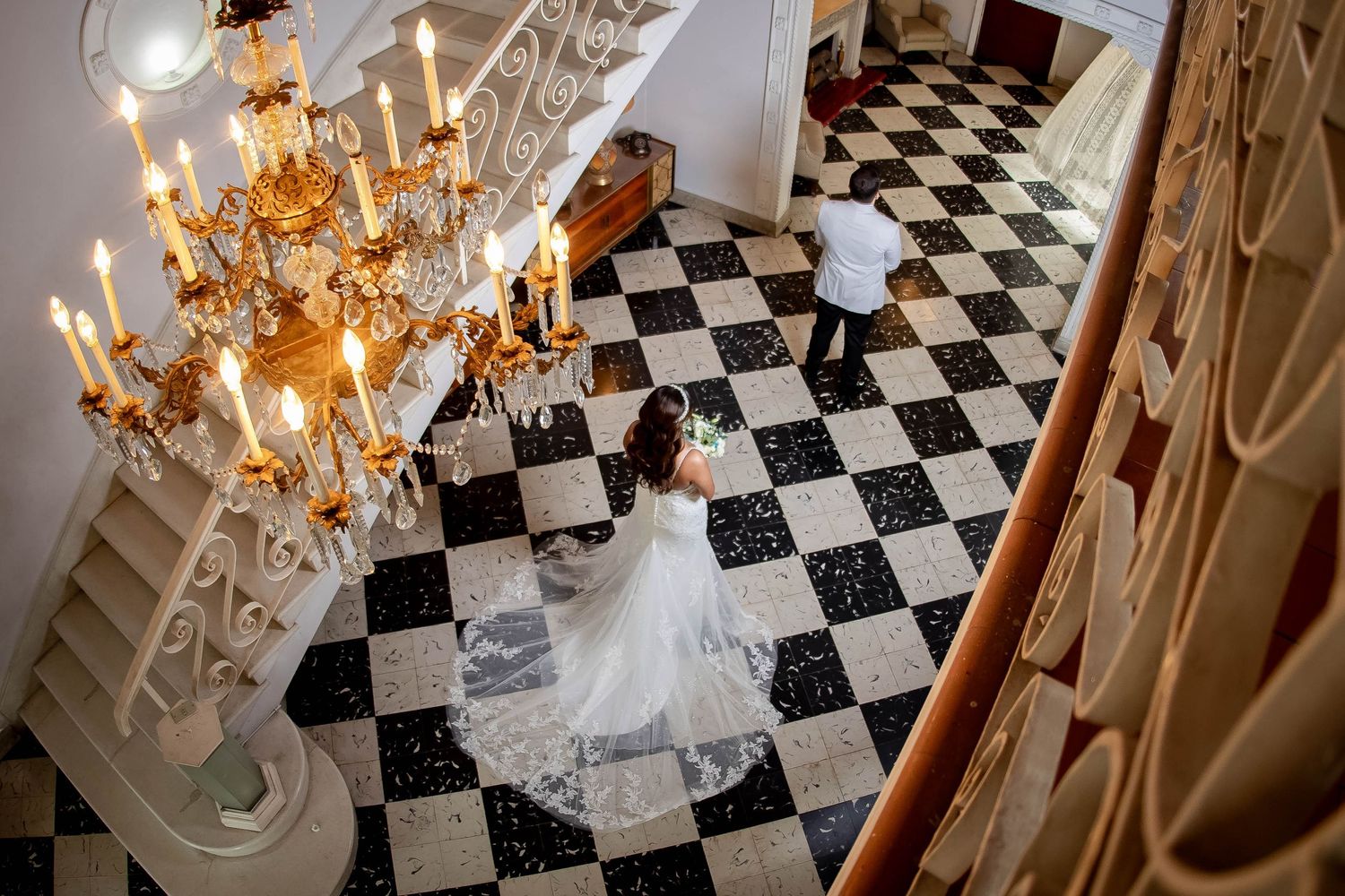 Elegant black and white checkered floor beneath crystal chandelier in grand ballroom setting.