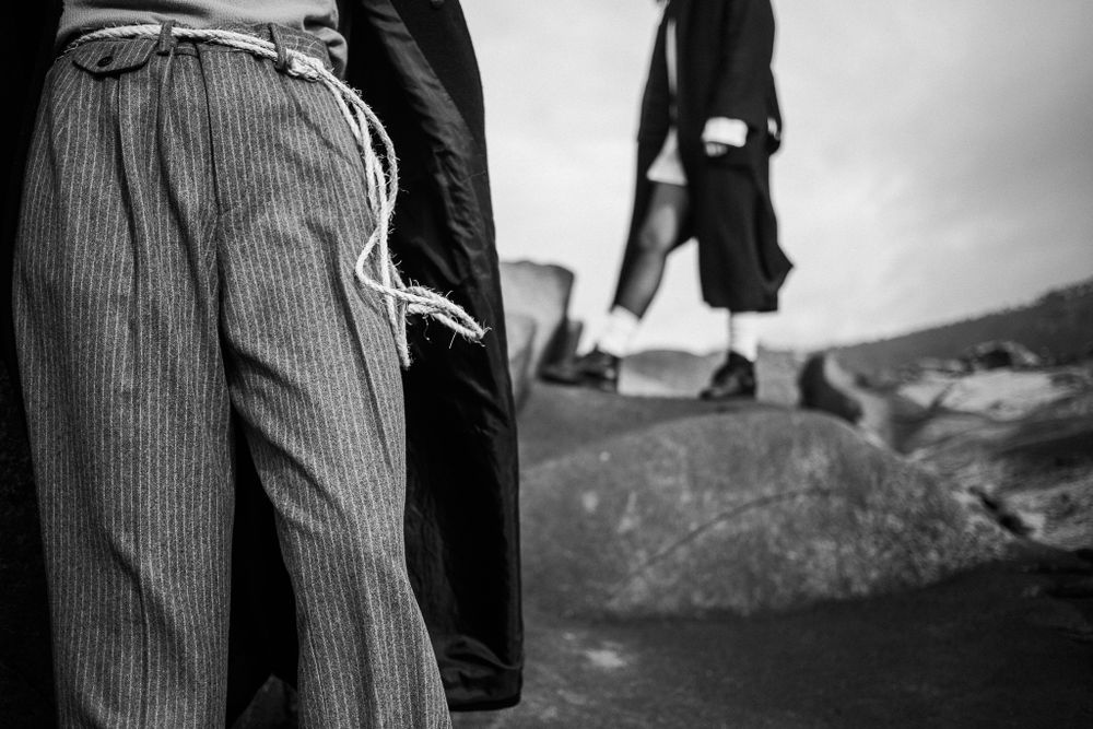Black and white artistic photograph showing striped trousers and coat silhouettes against a rocky landscape background.
