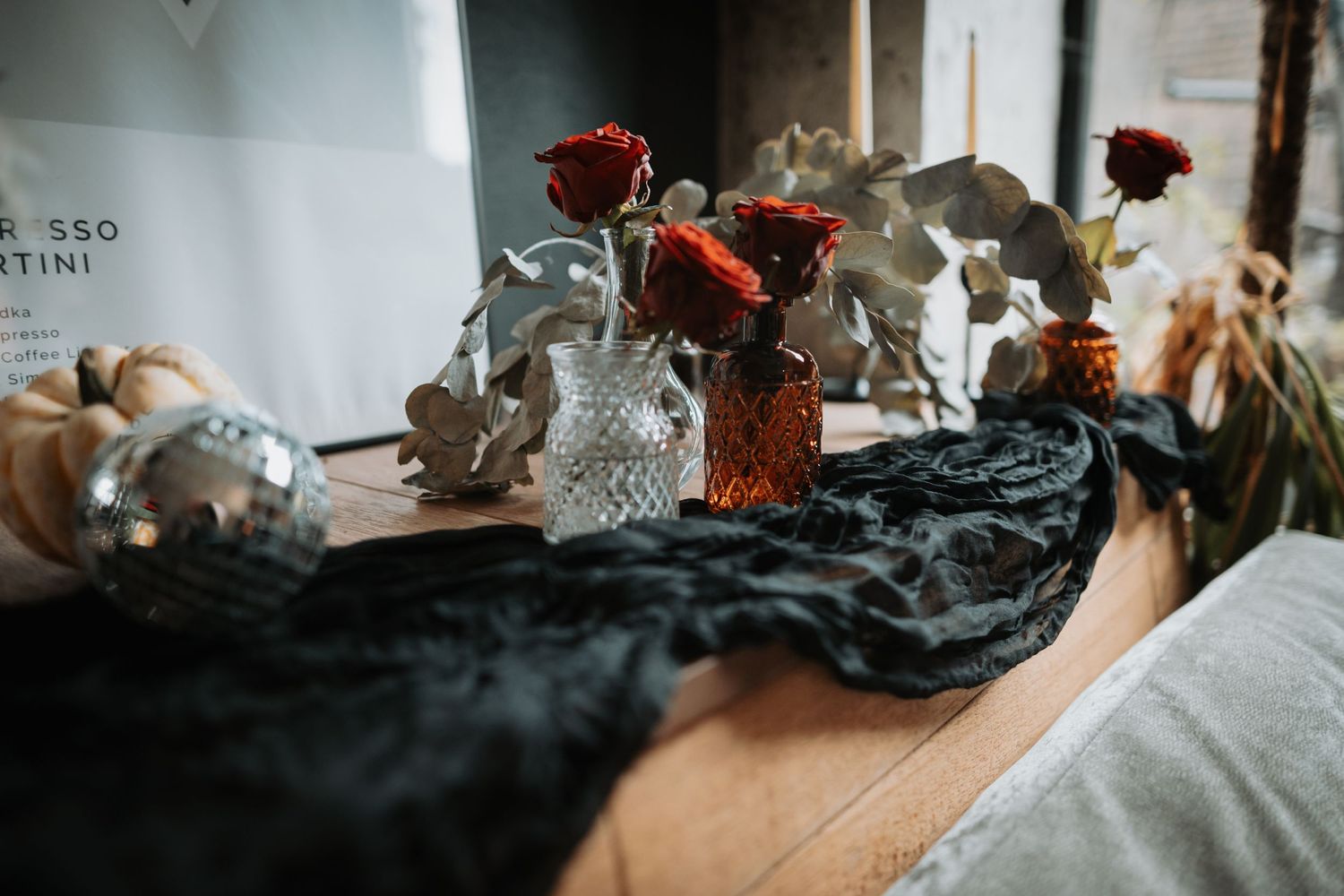 Red roses in crystal vases sit on dark fabric in a moody, romantic setting with soft lighting.