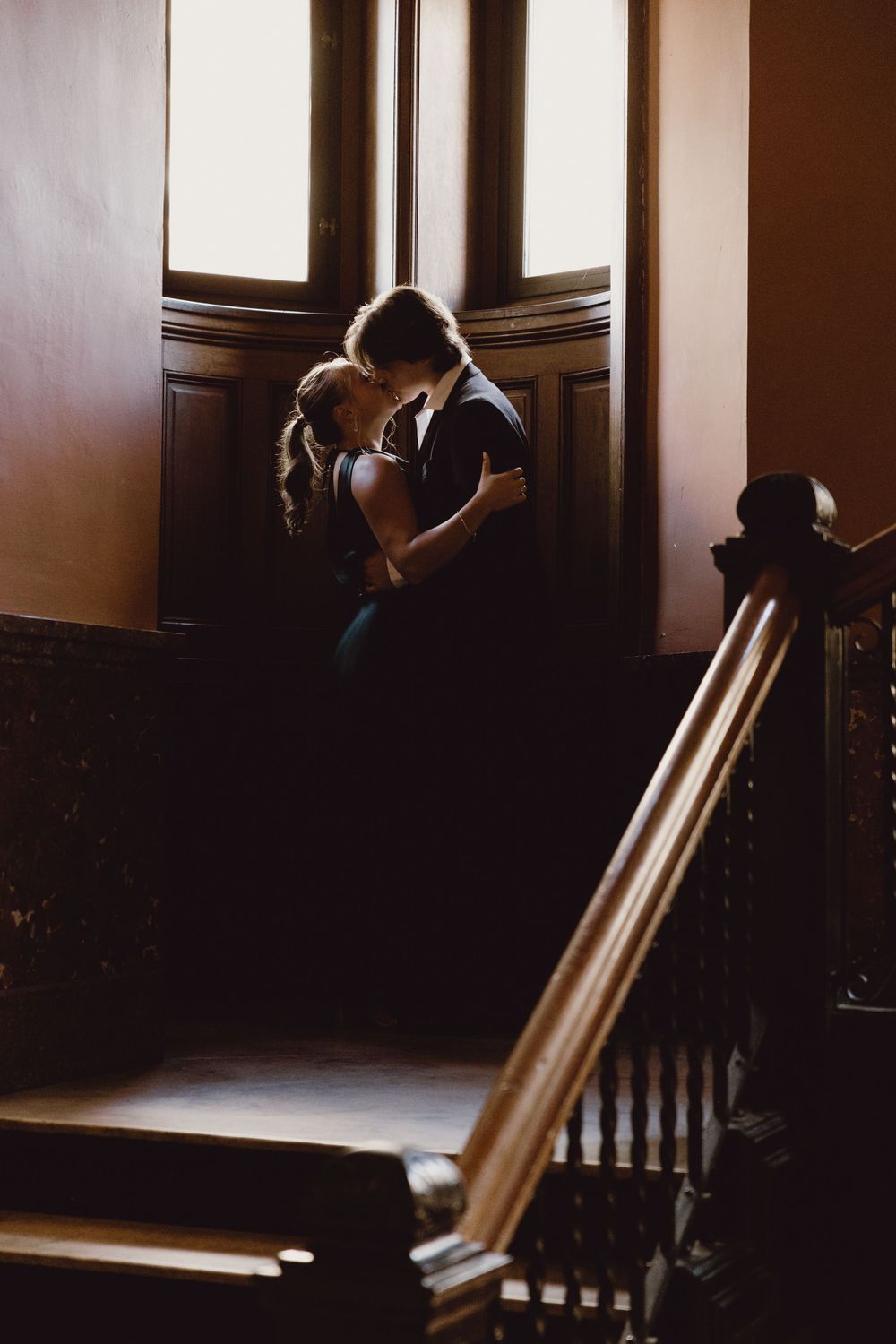 A romantic couple embraces in a dimly lit hallway with wooden paneling and dramatic shadows.