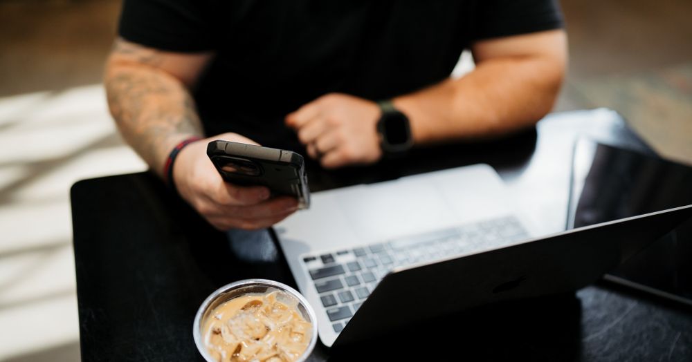 Person working on laptop with iced coffee and smartphone on desk.