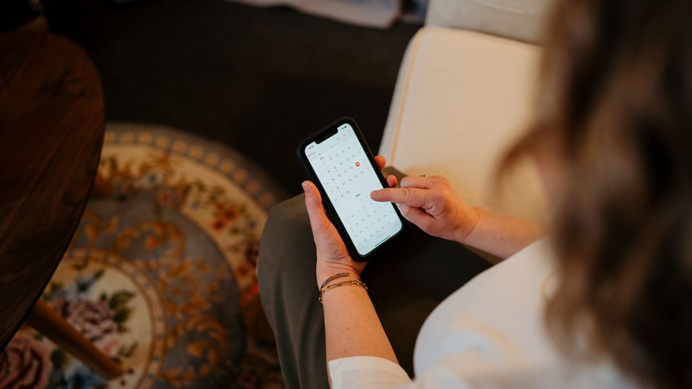 Hands holding a smartphone over a decorative patterned cushion or rug.