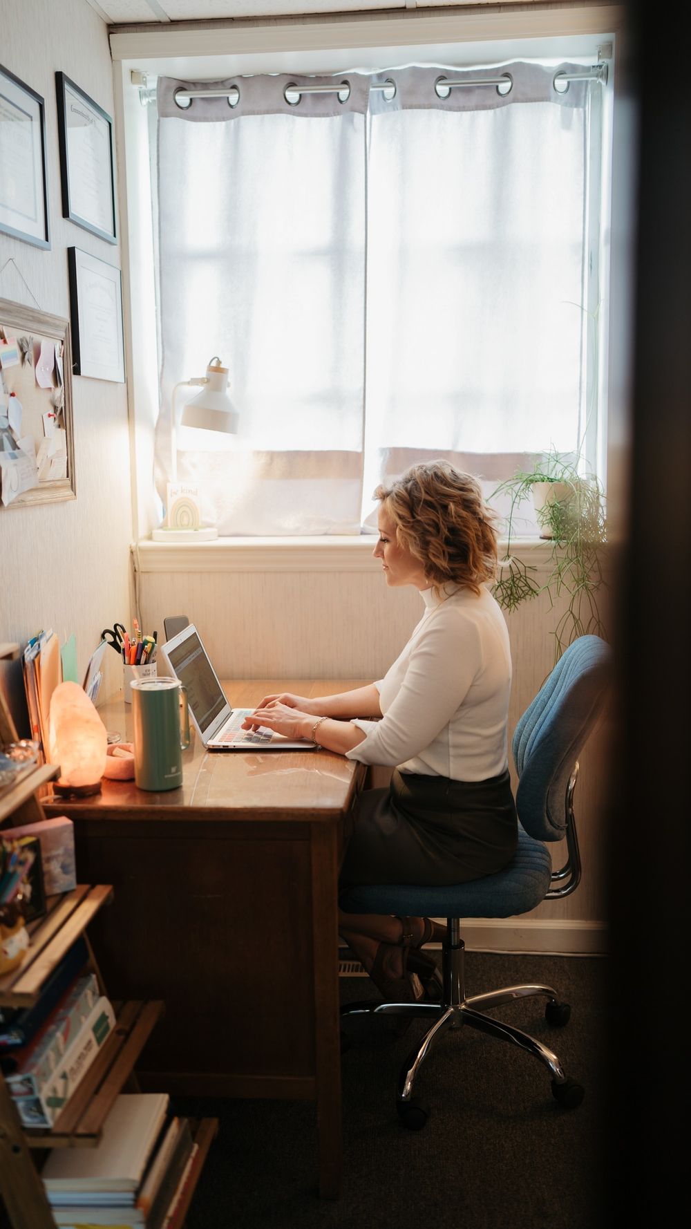 Person working at desk by window with natural light streaming in and office supplies.