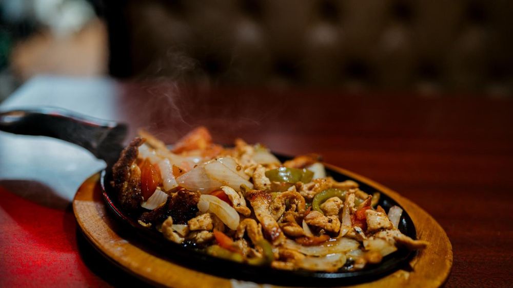 Sizzling fajitas served on a wooden platter with grilled onions and peppers.