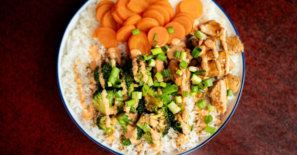 Rice bowl topped with grilled chicken, carrots, and fresh herbs.