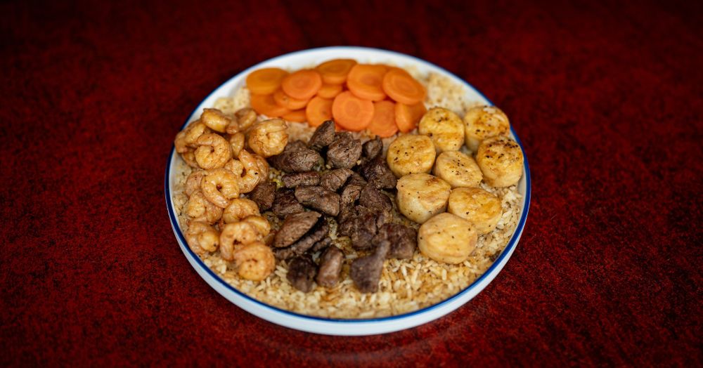Rice bowl with carrots, beef, and chicken arranged in neat sections.