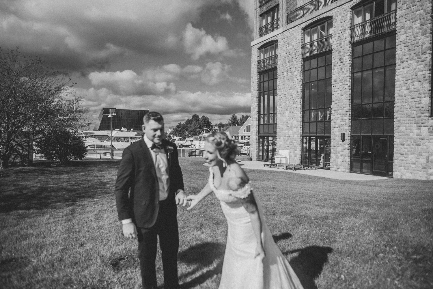 A black and white wedding photograph outside a historic brick building with dramatic clouds.