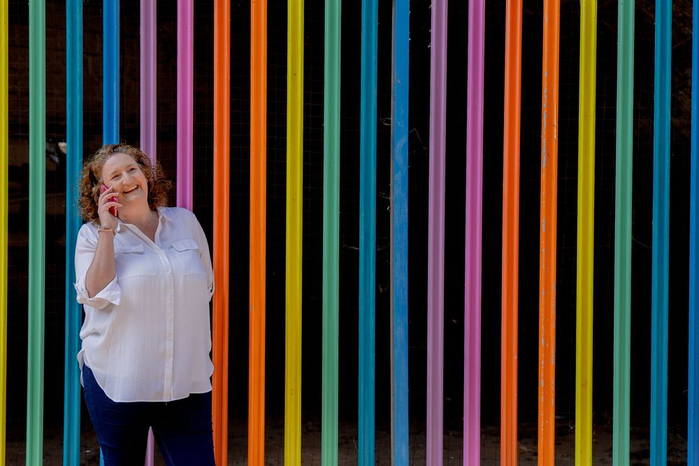 A person stands against a vibrant rainbow-striped background wall while talking on a mobile phone.