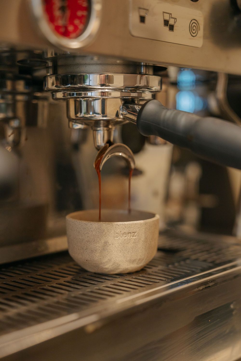 Close-up view of espresso dripping from a commercial coffee machine portafilter into a ceramic cup.