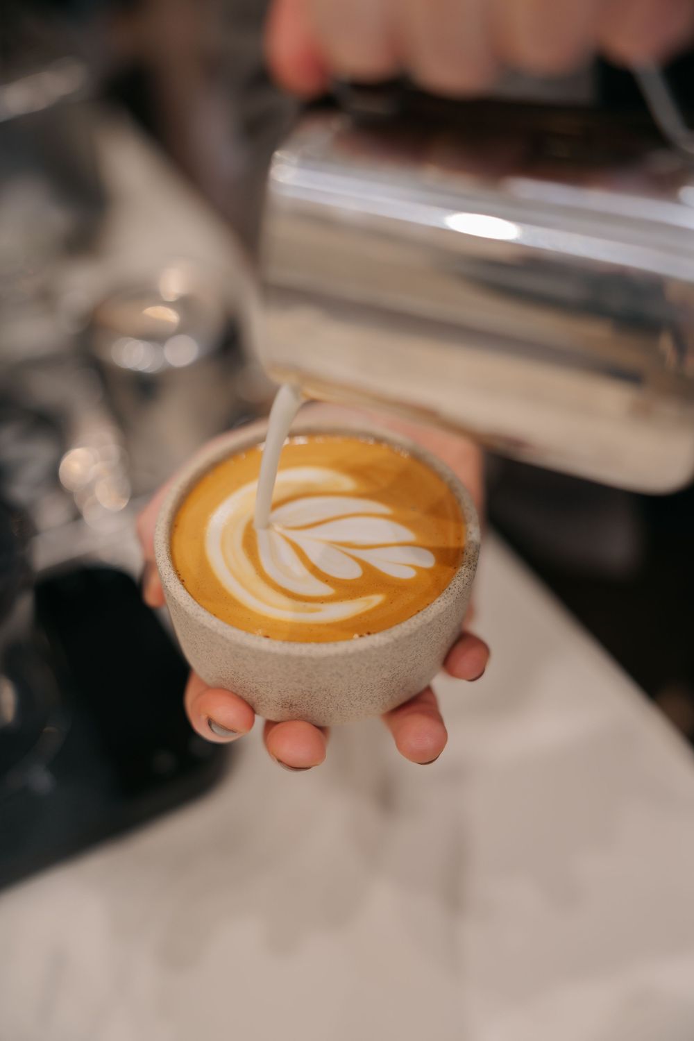 A sequence of latte art being poured into ceramic coffee cups showing tulip and rosetta patterns in golden foam.